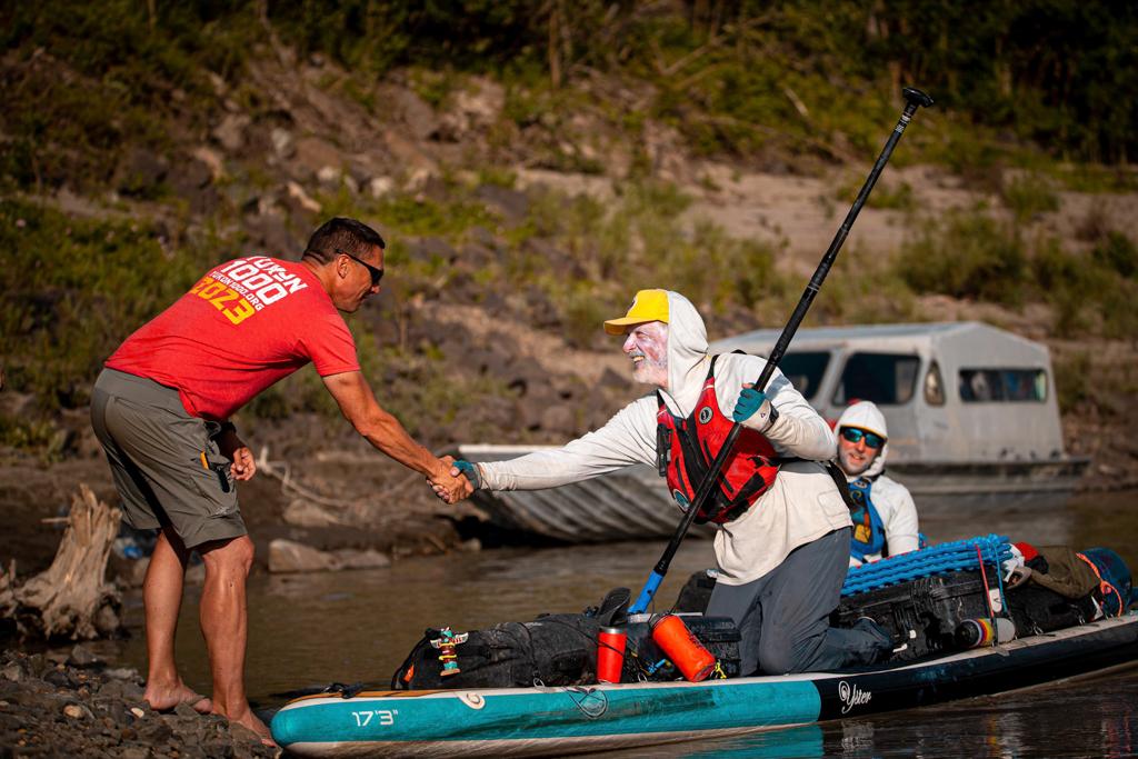 Two expedition paddlers shaking hands on a remote river — partnership and shared experience